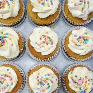 A number of vanilla cupcakes with sprinkles in a tray