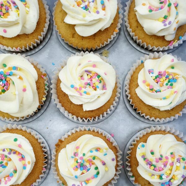 A number of vanilla cupcakes with sprinkles in a tray